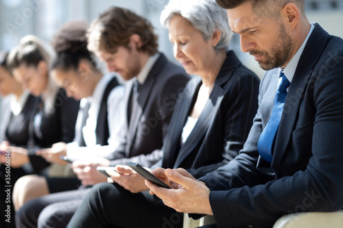 Group of business people with smartphones sitting in a row