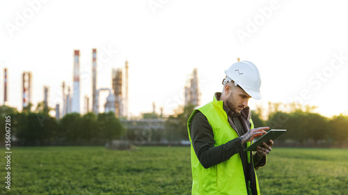 Young engineer with tablet standing outdoors by oil refinery. Copy space.