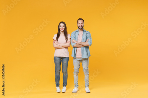 Smiling young couple two friends guy girl in pastel blue casual clothes posing isolated on yellow wall background studio portrait. People lifestyle concept. Mock up copy space. Holding hands crossed.