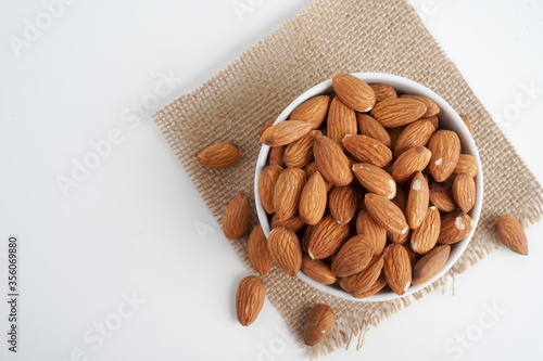 almonds in white bowl and glass of milk and brown fabric on white background. top view and flat lay, 