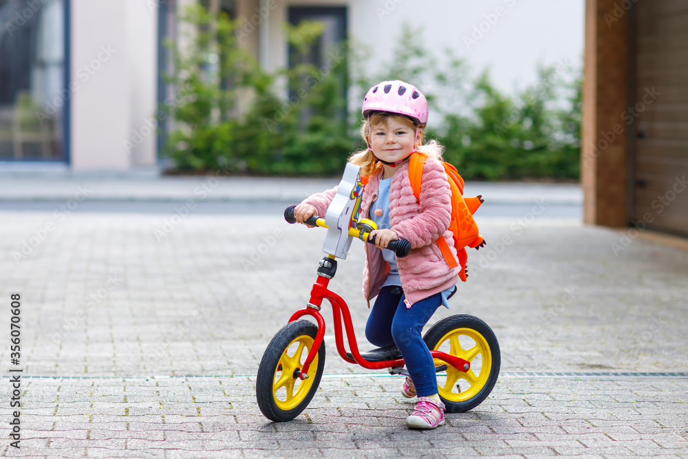 Little happy toddler girl on first day going to playschool daycare. Healthy baby on pushing bike to nursery school. Back to kindergarten after quarantine time from corona and covid 19 pandemic disease Little happy toddler girl on first day going to playschool daycare. Healthy baby on pushing bike to nursery school. Back to kindergarten after quarantine time from corona and covid 19 pandemic disease