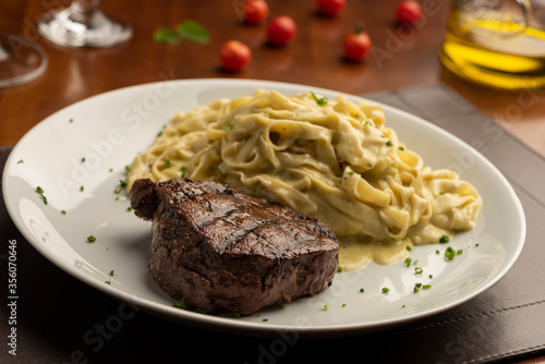 steak with pasta tagliatelle fetuccini on plate with blurred background with tomatoes olive oil and wine glass
