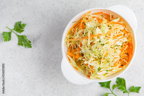 Photos Fresh coleslaw salad with cabbage and carrots in white bowl, top view
