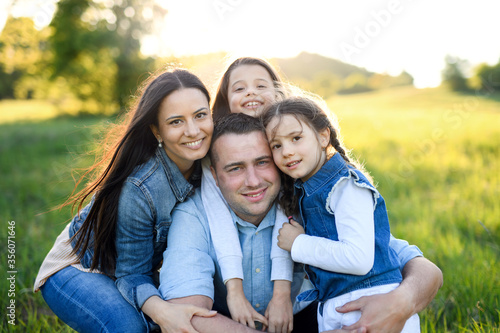 Happy family with two small daughters sitting outdoors in spring nature, looking at camera.