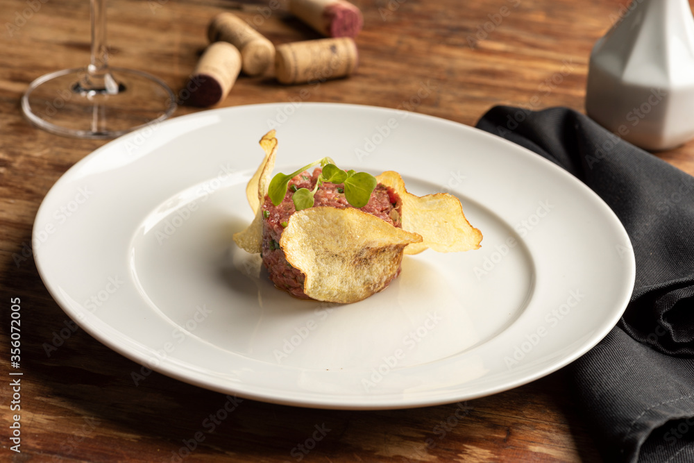 Steak tartare with potato chips on white plate and blurred background