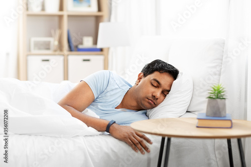 people, bedtime and rest concept - indian man with health tracker sleeping in bed at home