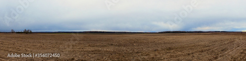Plowed field on a cloudy evening. Agro-industrial landscape. Panorama.