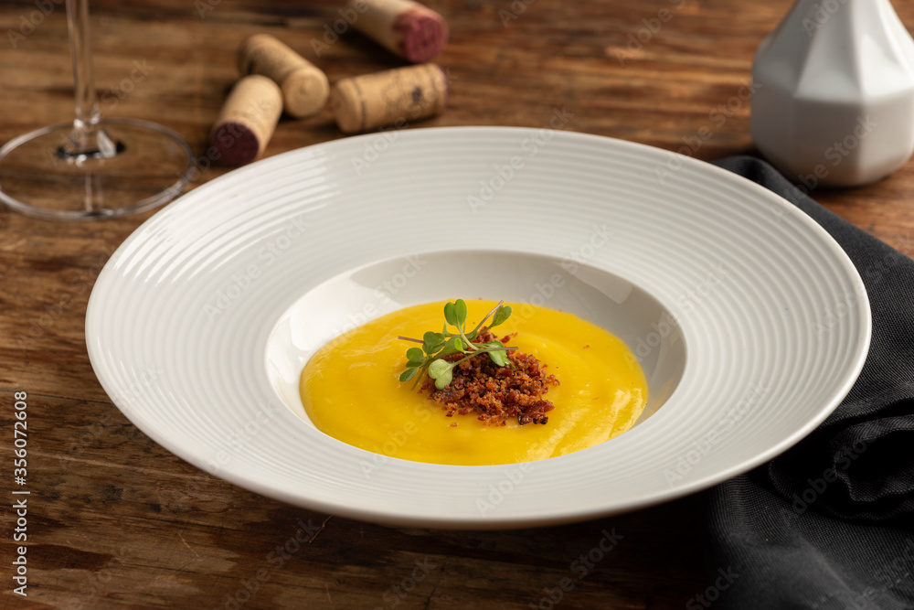 carrot, parsnip, pumpkin cream with bacon on white plate wooden table
