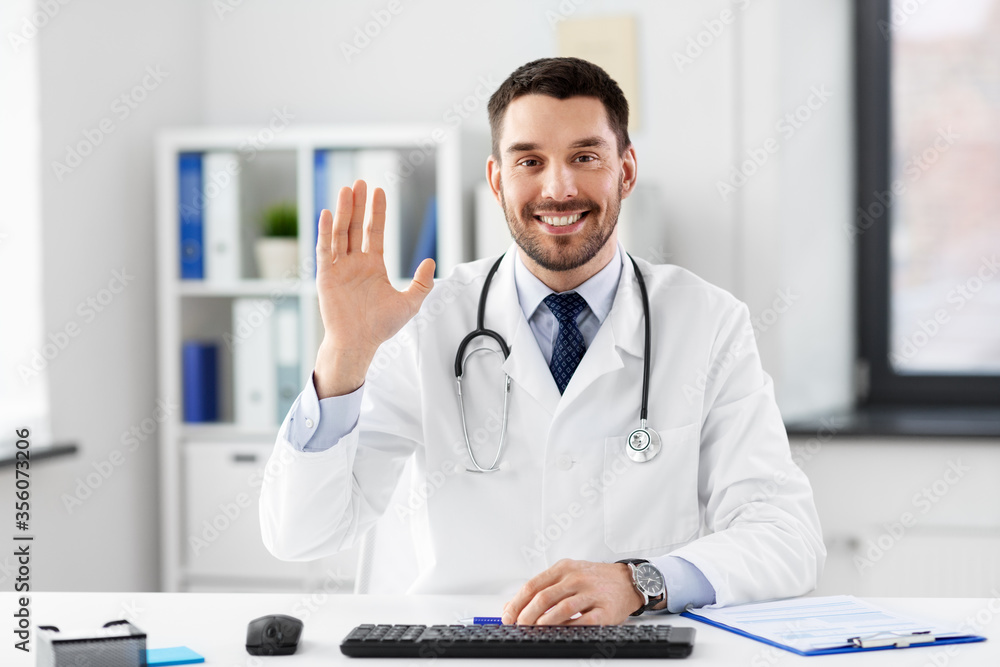 healthcare, medicine and people concept - happy smiling male doctor with stethoscope waving hand at hospital