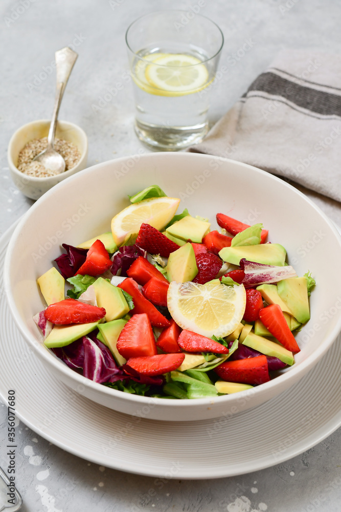 keto avocado salad with strawberry and lettuce leaves, a glass of water with lemon. food healthy breakfast or lunch. salad in a white bowl, top view.