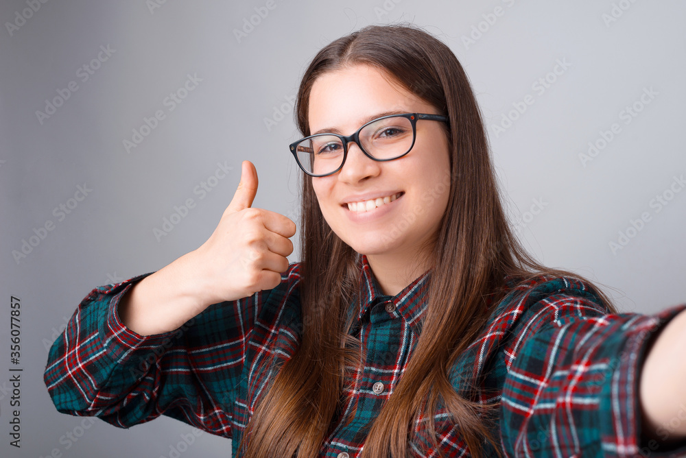 Portrait of happy young woman taking selfie and showing thumb up over white wall. Portrait of happy young woman taking selfie and showing thumb up over white wall.