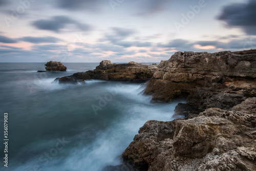 Amazing long exposure seascape with rocky beach and stormy sea at sunrise in the blue hour