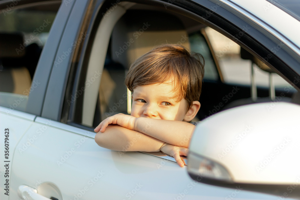 Boy looking out the window of the car,waiting to go on road trip.Cute little boy looking out of the car enjoying road trip with his father.Beautiful toddler leaning over the car door and looking away. Boy looking out the window of the car,waiting to go on road trip.Cute little boy looking out of the car enjoying road trip with his father.Beautiful toddler leaning over the car door and looking away.