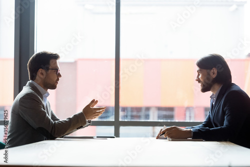 Foto Side view two businessmen talking at negotiations solve current issues, sales manager make offer to client speaking sit at desk
