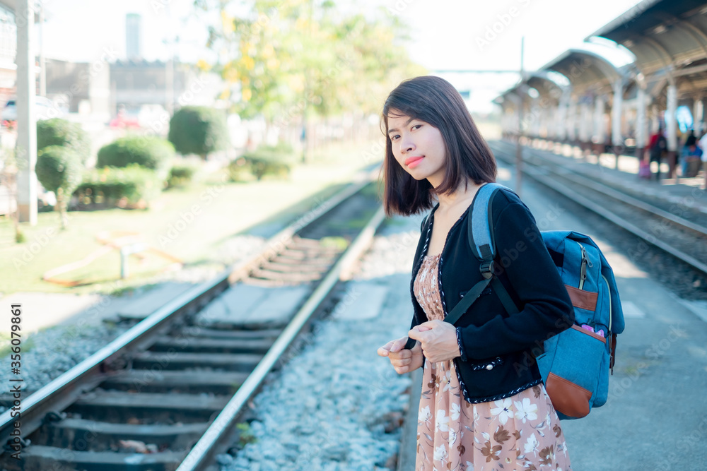Asian woman tourists is standing on a backpack. Wait for the train to travel. On vacation.