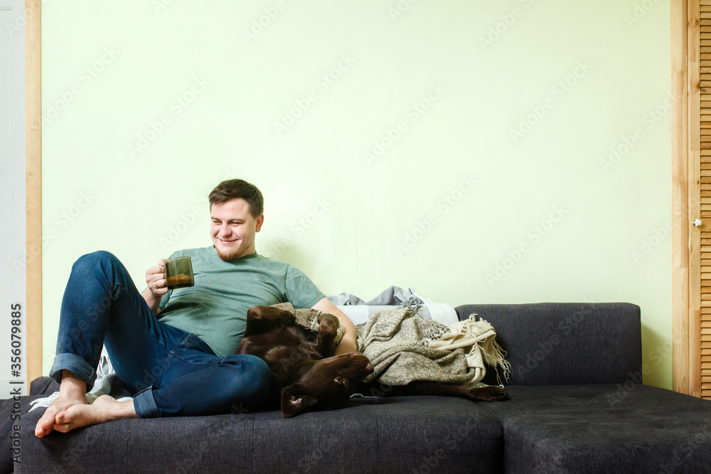 Happy handsome man sitting on the couch at home with pet dog labrador retriever Happy handsome man sitting on the couch at home with pet dog labrador retriever