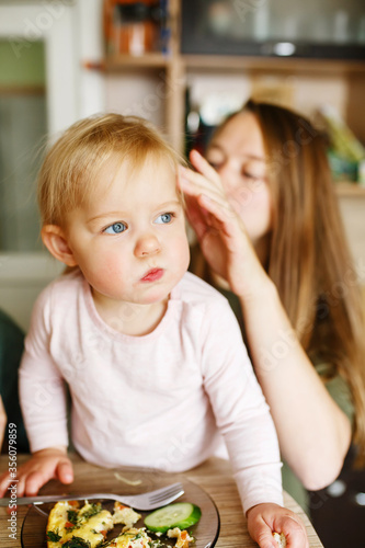 Young mother with her infant daughter at home kitchen having breakfast