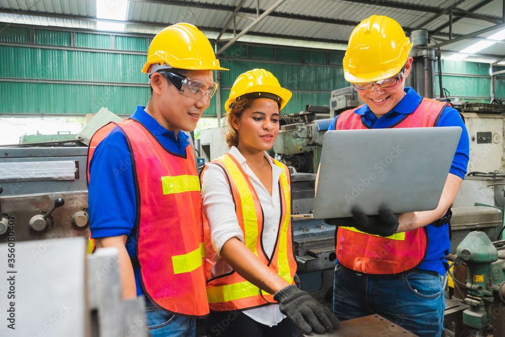 Engineering team, men and women, wearing helmets, brainstorming projects with laptops in industrial factories Engineering team, men and women, wearing helmets, brainstorming projects with laptops in industrial factories