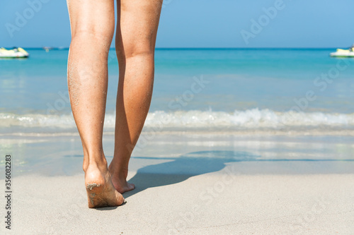 Young Asian woman walking on sand beach. Closeup detail of female feet and white sand at Phuket, Thailand. Beach travel concept.