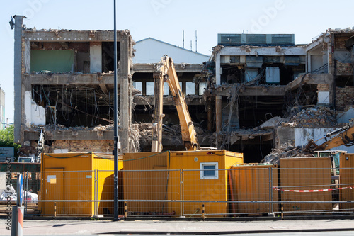 Bauarbeiten Abbrucharbeiten eines großen Gebäudes, im Vordergrund sind ein Bauzaun und gelbe Baucontainer