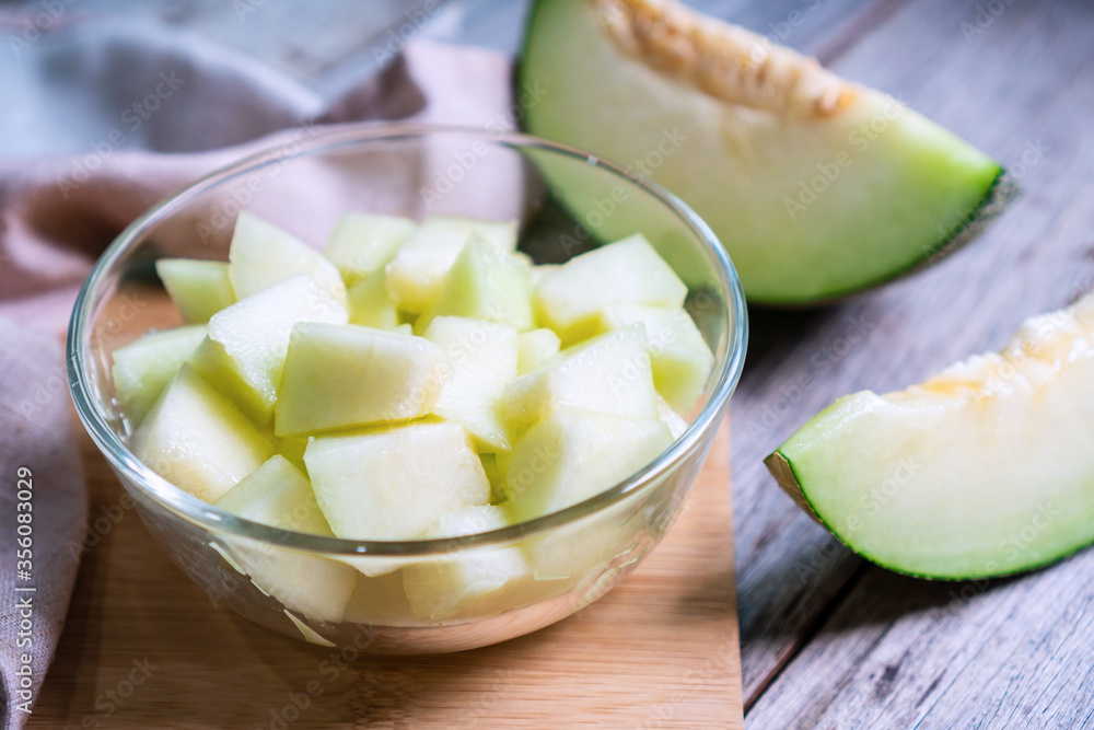 Cut of fresh sweet green melon in bowl glass on the wooden table. Fruits or healthcare concept. Selective focus, close up Cut of fresh sweet green melon in bowl glass on the wooden table. Fruits or healthcare concept. Selective focus, close up