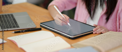 Female college student doing her assignment with mock-up tablet, laptop and stationery on library desk