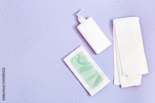 Green waxing strips with mint and cooling effect, body moisturizer and white cotton towel on blue paper background with copy space. Flat lay.