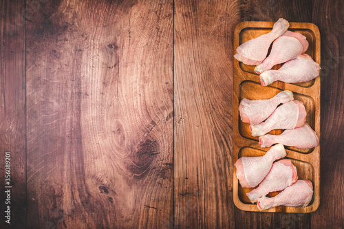 A wooden board full of FRESH RAW ORGANIC CHICKEN DRUMSTICK on the table with free space for text/decoration.