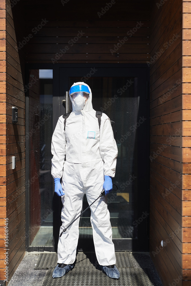 Vertical full length portrait of male worker wearing protective suit standing against door with disinfecting equipment