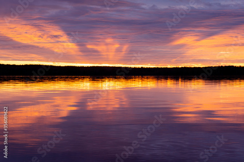 Water surface. Sunset sky background. Gold sunset sky with evening sky clouds over the lake. Small waves. Water reflection © Anna
