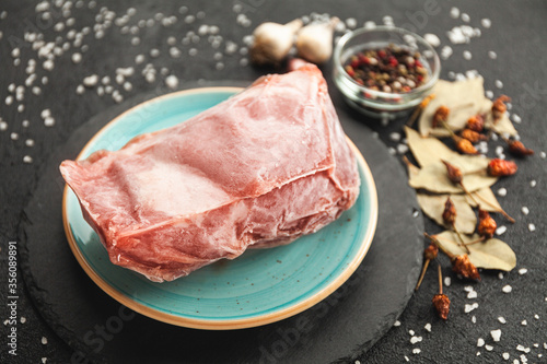 Frozen piece of raw meat on plate on black table. Rime on product, thawing.