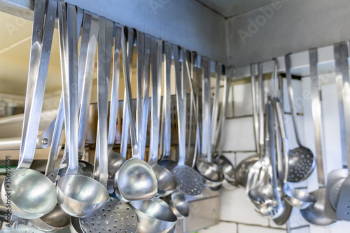 close up view of many soup ladles hanging from a wall rack in a restaurant kitchen