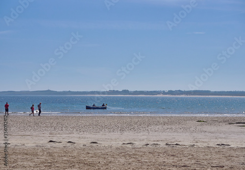 A Small Wooden Local Fishing Boat with 2 Fishermen laying its nets close to the Beach at Beadnell Bay in Northumberland, England, UK.