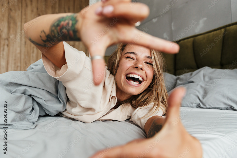 Image of woman making photo frame sign with fingers while lying in bed - obrazy, fototapety, plakaty 