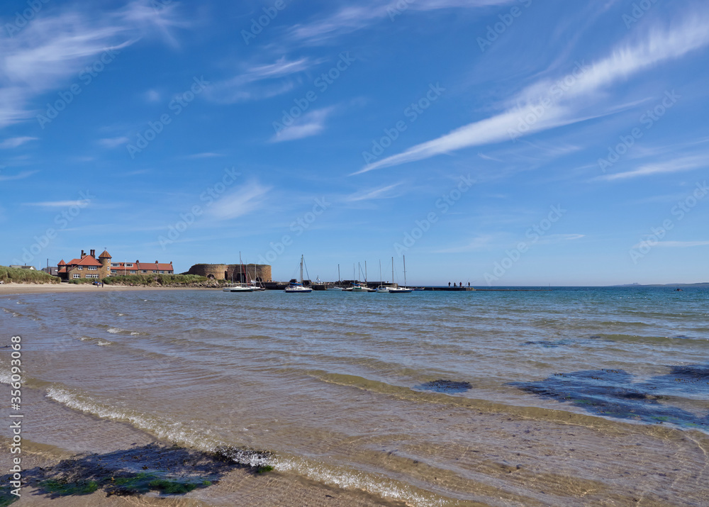 A Landscape photo of Beadnell Bay and Beach looking towards the Harbour and Old Lime Kilns in Northumberland, England, UK.