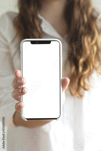 Mock up of last smartphone with a blank screen in female hands on a light home background. 