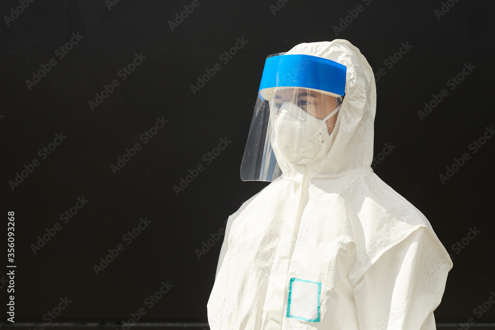 Chest up portrait of female worker wearing full protective suit standing against black background and looking away, disinfection and virus protection concept, copy space