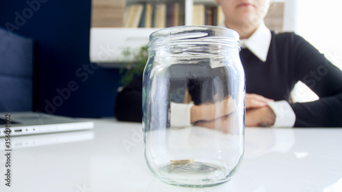 Closeup image of business lady dressed in black dress ,sitting at the white table on which is located empty of coints jar photo