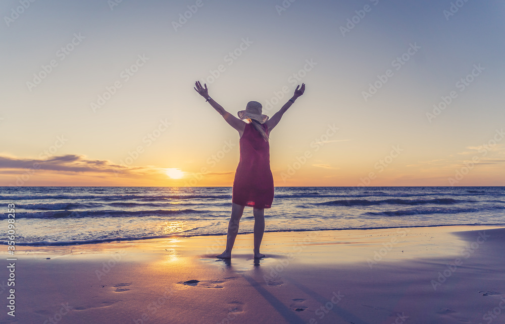 Woman in red with arms outstretched by the sea at sunrise enjoying freedom and outdoors life