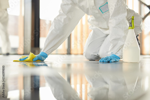 Close up of unrecognizable worker wearing protective suit cleaning floor with chemicals during disinfection indoors, copy space photo