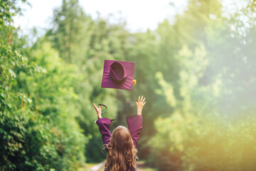 Photo from back graduate graduated little girl in cap throw it up in the sky, happy of ending, violet costume