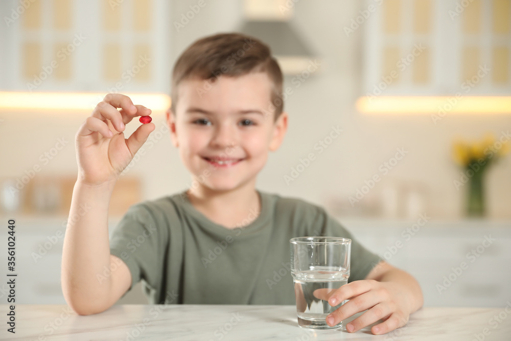 Little boy with glass of water and vitamin capsule in kitchen, focus on hands Little boy with glass of water and vitamin capsule in kitchen, focus on hands