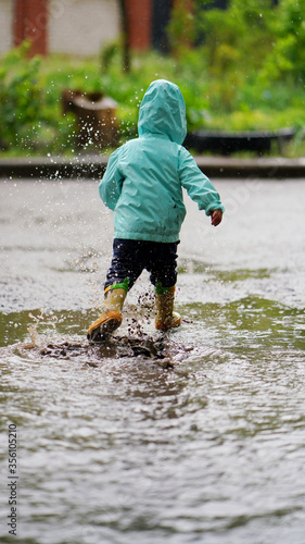 Fototapeta Naklejka Na Ścianę i Meble -  Portrait of a funny little boy in a hood walking through a puddle