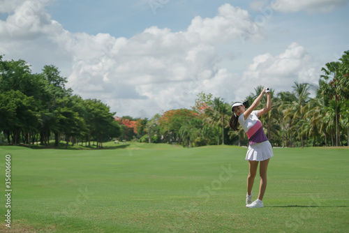 Asian female golfer swinging club on golf course green with copy space.