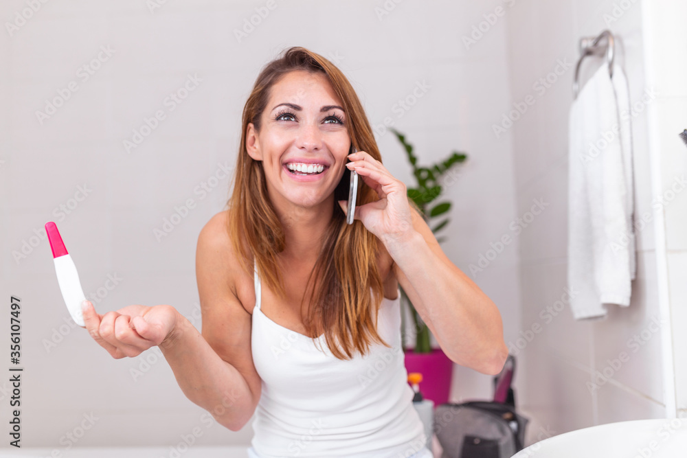 Smiling young woman looking on pregnancy test. Happy woman with pregnancy test. Smiling girl telling good news on mobile. Family, child expectation and maternity concept. Copy space Smiling young woman looking on pregnancy test. Happy woman with pregnancy test. Smiling girl telling good news on mobile. Family, child expectation and maternity concept. Copy space