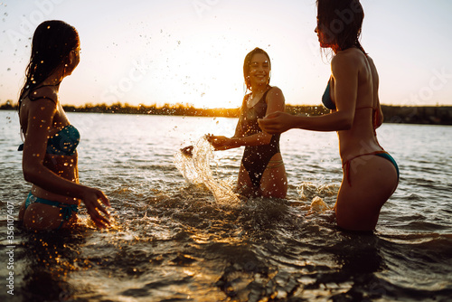 Young girls squirting and having fun in the sea at sunset. Beach holiday and summer vacation concept.