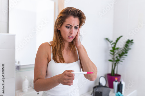 Shocked woman looking at control line on pregnancy test. Shocked young girl with unwanted pregnancy looking the test in the bathroom. sad young woman holding pregnancy test feeling hopeless