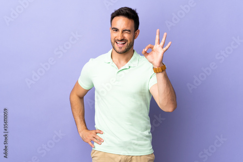 Young handsome man isolated on purple background showing ok sign with fingers