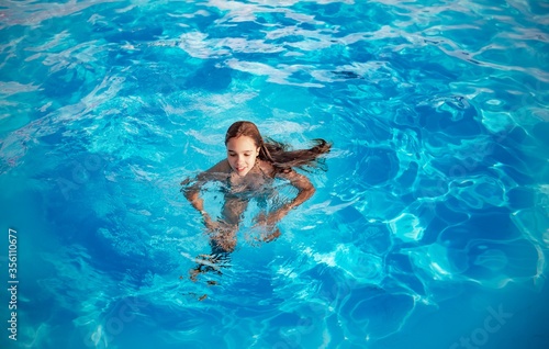 Teenage girl swims in the clear blue water of a pool during a vacation in a warm tropical country on a sunny warm summer day. Travel concept. Advertising space © YouraPechkin
