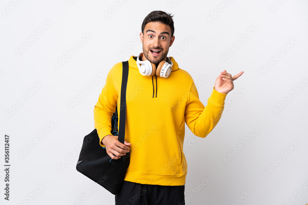 Young sport man with sport bag isolated on white background surprised and pointing finger to the side Young sport man with sport bag isolated on white background surprised and pointing finger to the side